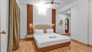 A modern hotel room with a large bed, wooden flooring, a ceiling fan, and a wooden panel wall.
