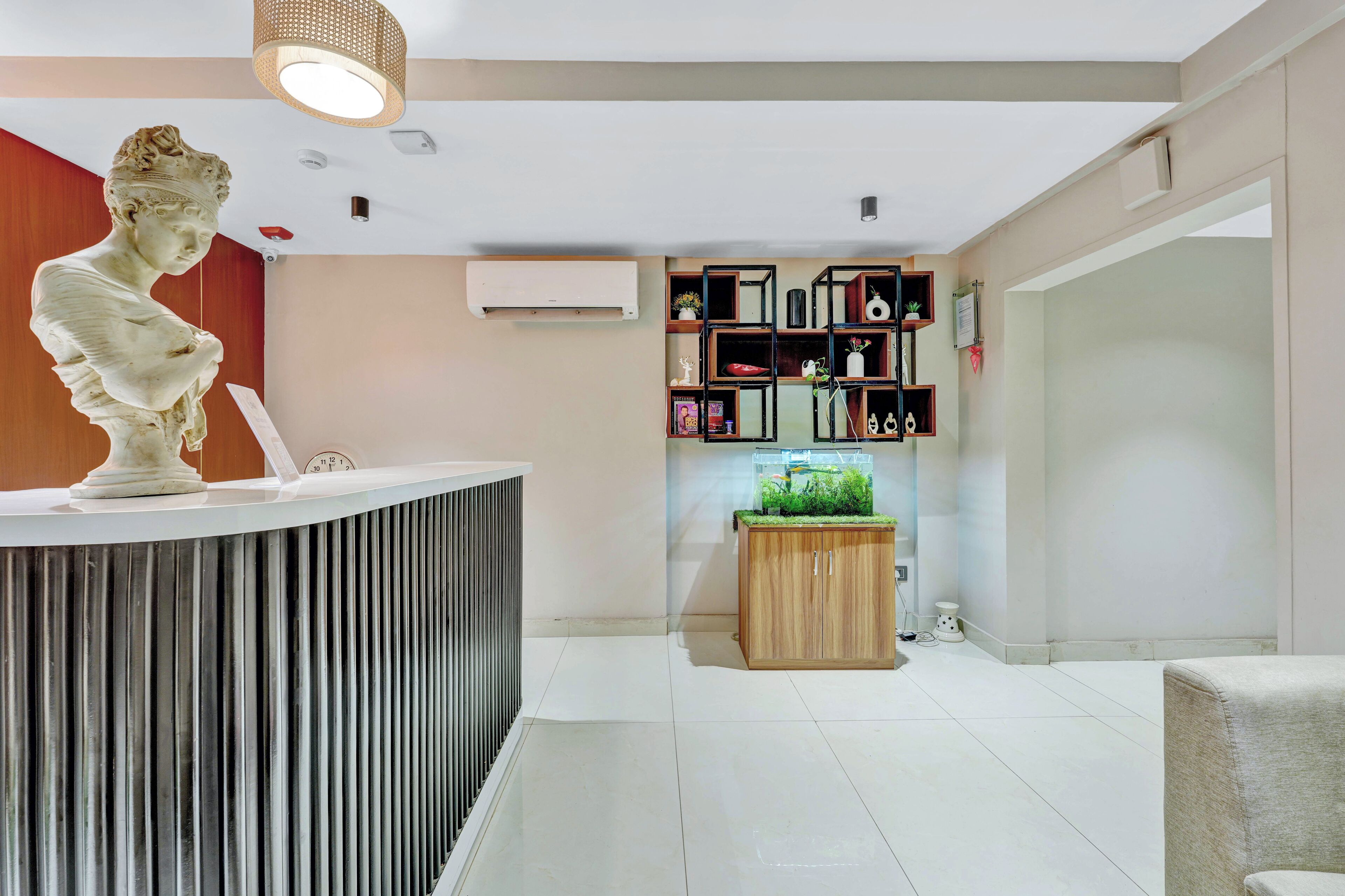 A reception area with a marble bust, a wooden cabinet with a plant, and a modern shelving unit with various items.