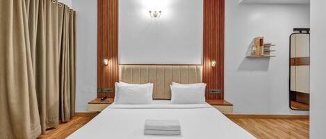 Una habitación de hotel moderna con una cama grande, paneles de madera, una mesita de noche con lámpara y un espejo en la pared.