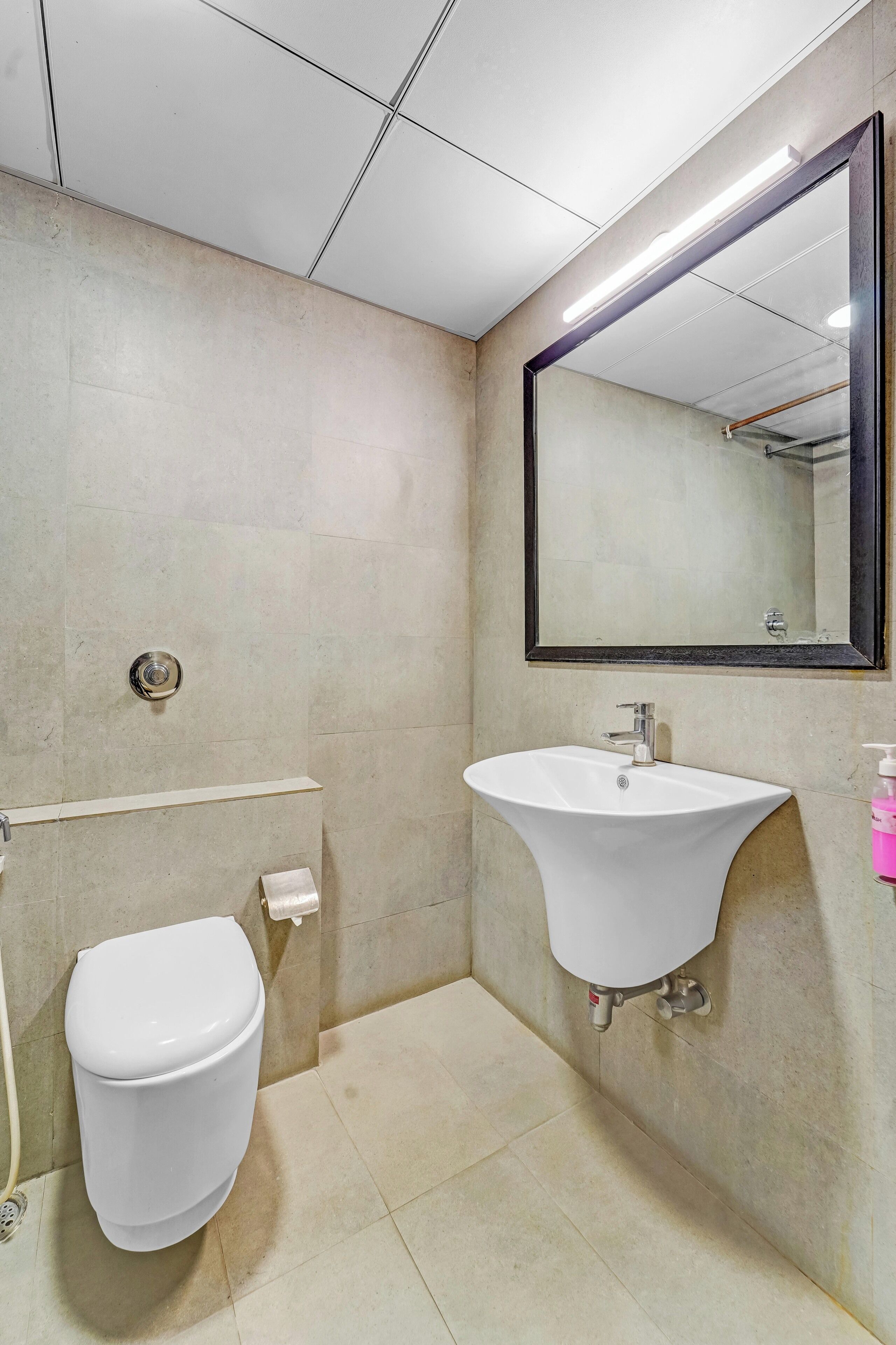 A bathroom with a toilet, sink, mirror, and tiled walls.