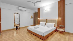 Quarto moderno com uma cama grande, piso de madeira, ventilador de teto, espelho e mesa de cabeceira com abajur.