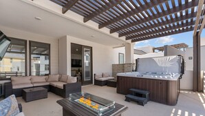 A covered outdoor living area with a glass-top fire feature, a hot tub, and comfortable seating.