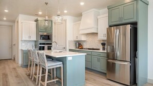 A modern kitchen with a central island, bar stools, stainless steel appliances, and light-colored cabinetry.