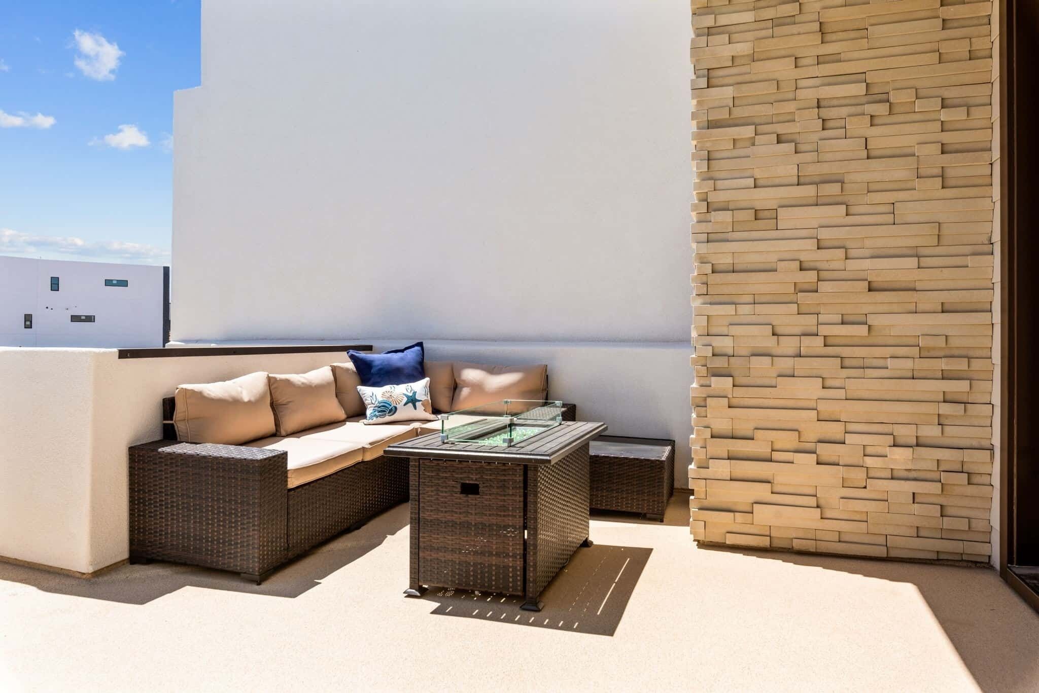 An outdoor seating area with a sofa, cushions, and a glass-top table.
