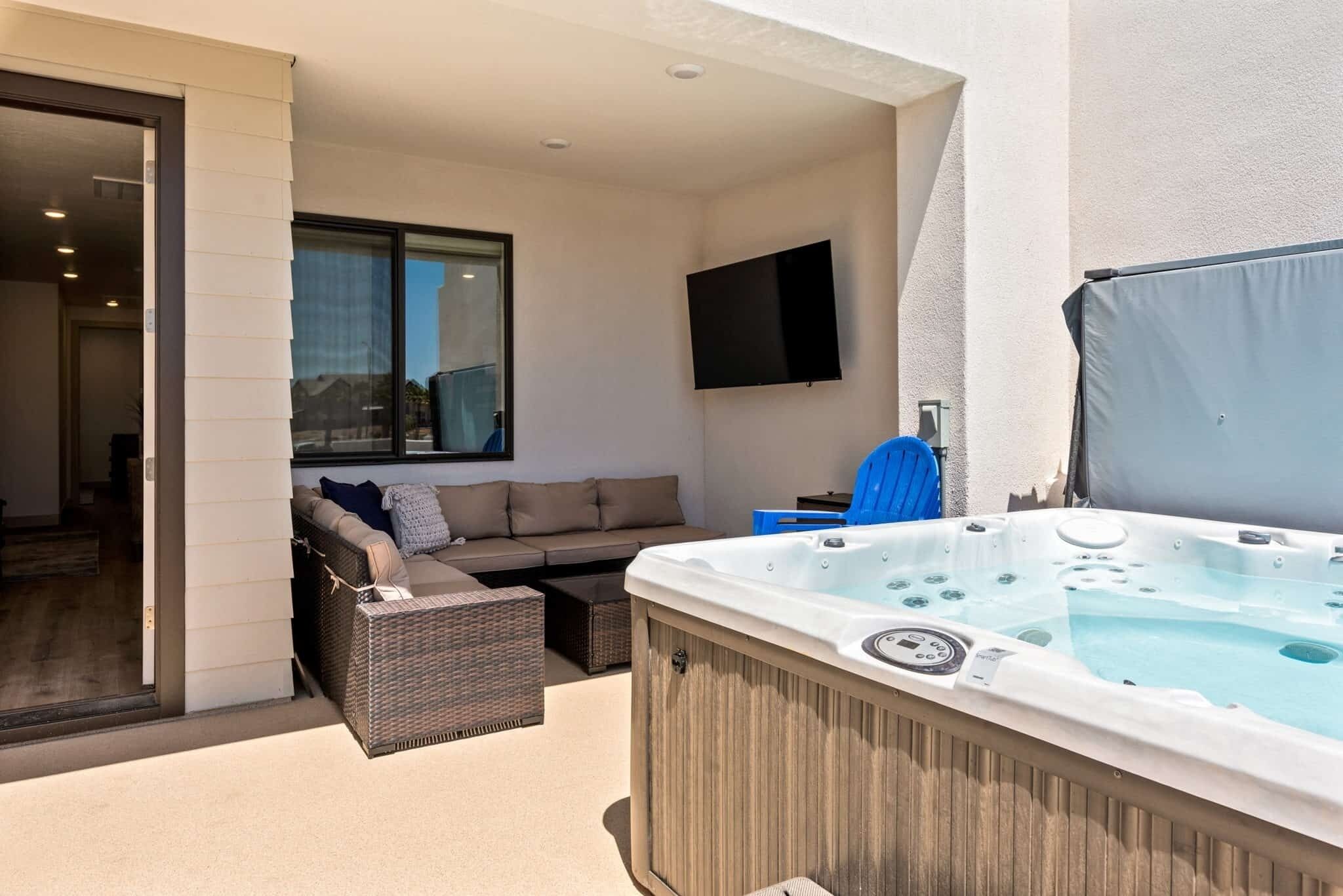 A modern outdoor living area with a hot tub, a sofa, and a flat-screen TV.