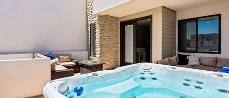 A rooftop patio with a hot tub, outdoor seating, and a stone wall.