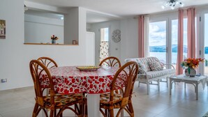 A dining area with a round table, wicker chairs, and a view of the sea through large windows. - Casetta Letizia in Portoferraio (Portoferraio)