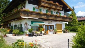 Un edifici d'estil alpí tradicional amb un balcó, espai exterior per seure i una zona de jardí.
