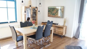 A dining area with a wooden table and chairs, pendant lights, a cabinet, and a painting on the wall. - Thatched roof house Hasel 2 (Poseritz)