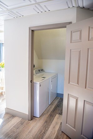 A laundry room with a washing machine and dryer, wooden flooring, and a white door. - The Masterson Tower: Spacious, Modern Stay (Cleveland)
