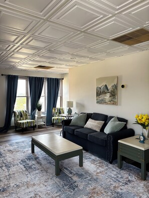 A living room with a dark sofa, a coffee table, a patterned armchair, and a painting on the wall. - The Masterson Tower: Spacious, Modern Stay (Cleveland)