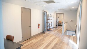A hallway with a wooden floor, a door, a fire extinguisher, a ladder, and an exit sign.