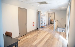 A hallway with a wooden floor, a door, a fire extinguisher, a ladder, and an exit sign. - The Masterson Tower: Spacious, Modern Stay (Cleveland)