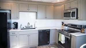 A kitchen with white cabinets, a stainless steel refrigerator, a microwave, a dishwasher, and an oven.