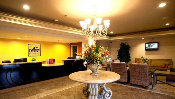 Un vestíbulo de hotel con un mostrador de recepción, una araña de cristal, una mesa redonda con un centro de mesa floral y una zona de estar con sofás y sillones.