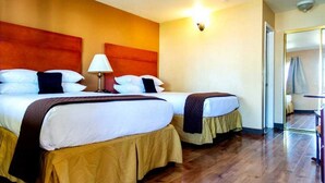 Una habitación de hotel con dos camas, una mesita de noche, una lámpara y un espejo.