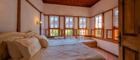 Un dormitorio con una cama grande, un banco y varias ventanas con cortinas.