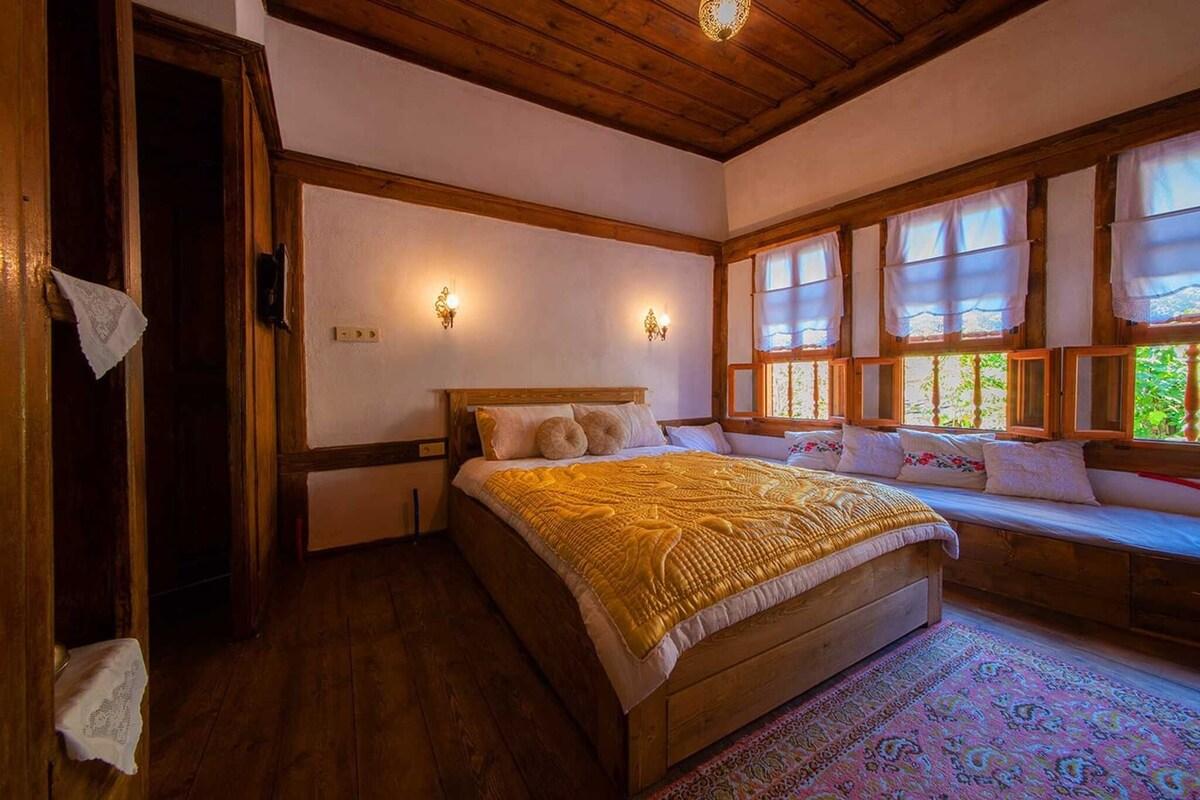 A bedroom with a wooden bed, two wall sconces, a window with curtains, and a patterned rug.