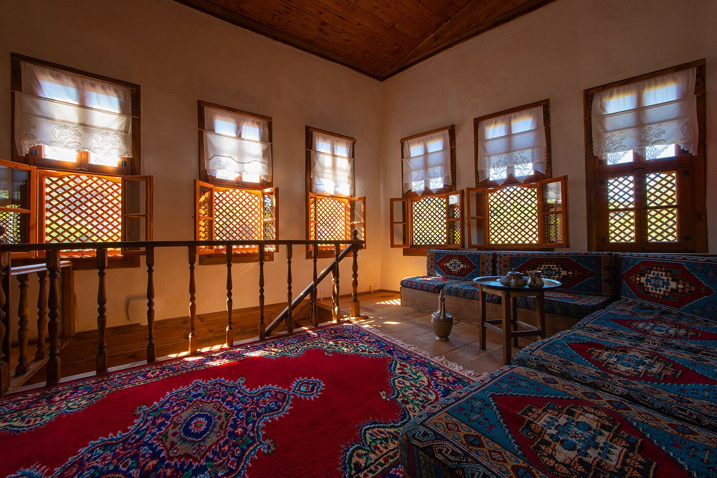 Une pièce au décor traditionnel, avec un escalier en bois, une moquette rouge à motifs et un canapé aux motifs complexes.