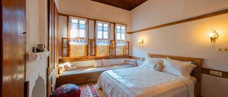 Une chambre confortable avec un plafond en bois, un grand lit recouvert de draps blancs, un banc agrémenté de coussins et une fenêtre ornée de rideaux en dentelle.
