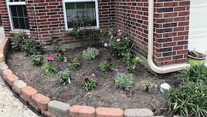 Ein Backsteinhaus mit einem Blumenbeet voller verschiedener Blumen und Pflanzen.