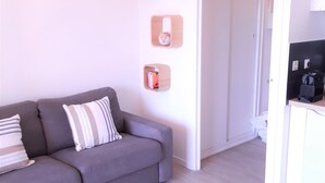 A modern living room with a grey sofa, a white lamp, and a small wooden shelf with a globe and books. - Lovely studio in private residence + parking. Beach, port and shops on foot (Cavalaire-sur-Mer)