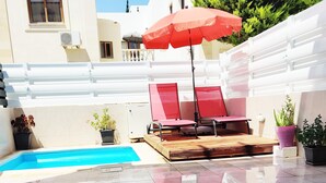 Zona de piscina amb una parasol vermell, dues gandules vermelles i plantes en testos.