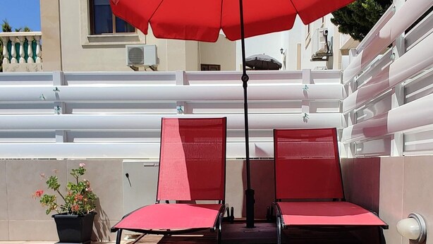 Zona de piscina amb dues gandules vermelles i un parasol vermell.
