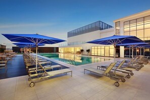 A poolside area with lounge chairs and umbrellas, a pool, and a modern building with large windows. - Noble Resort Hotel Melaka (Malacca City)