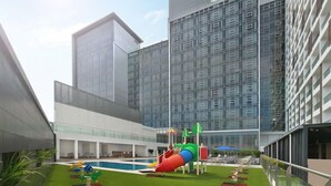 Un hotel moderno con piscina en la azotea y área de juegos que incluye un tobogán colorido y estructuras recreativas.