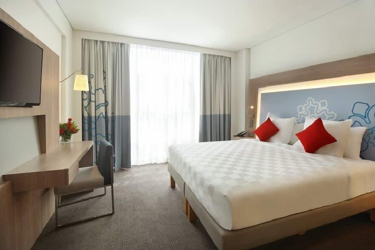 A hotel room with a bed, a desk, a chair, a TV, and a window with curtains.