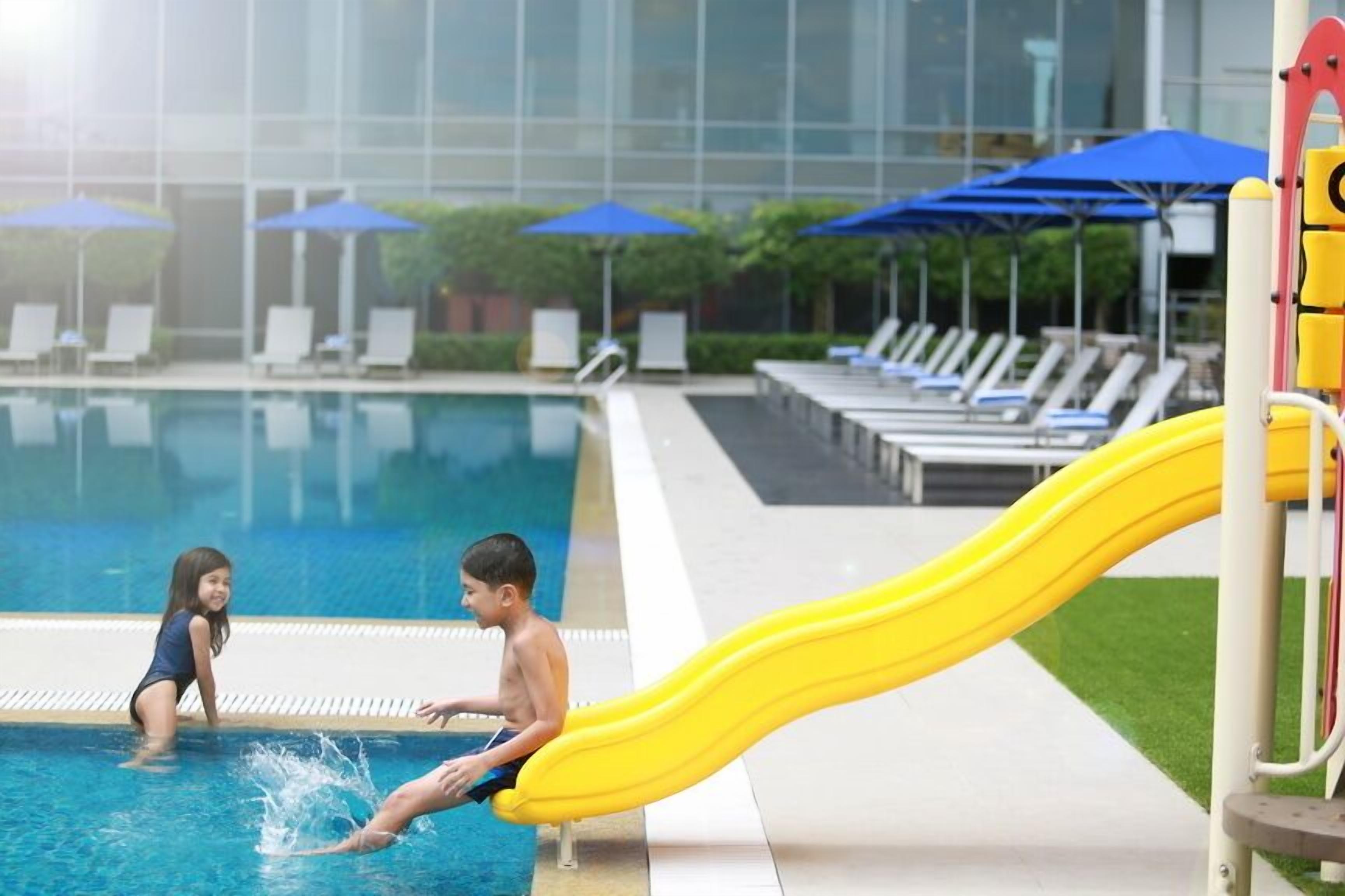 A swimming pool with a yellow slide and lounge chairs.