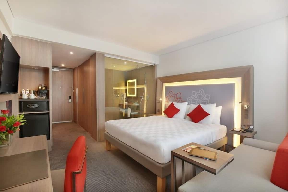 A modern hotel room with a large bed, a desk, a chair, and a small table.