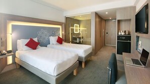 Habitación de hotel con dos camas, un escritorio con una computadora portátil, un televisor y un minibar.