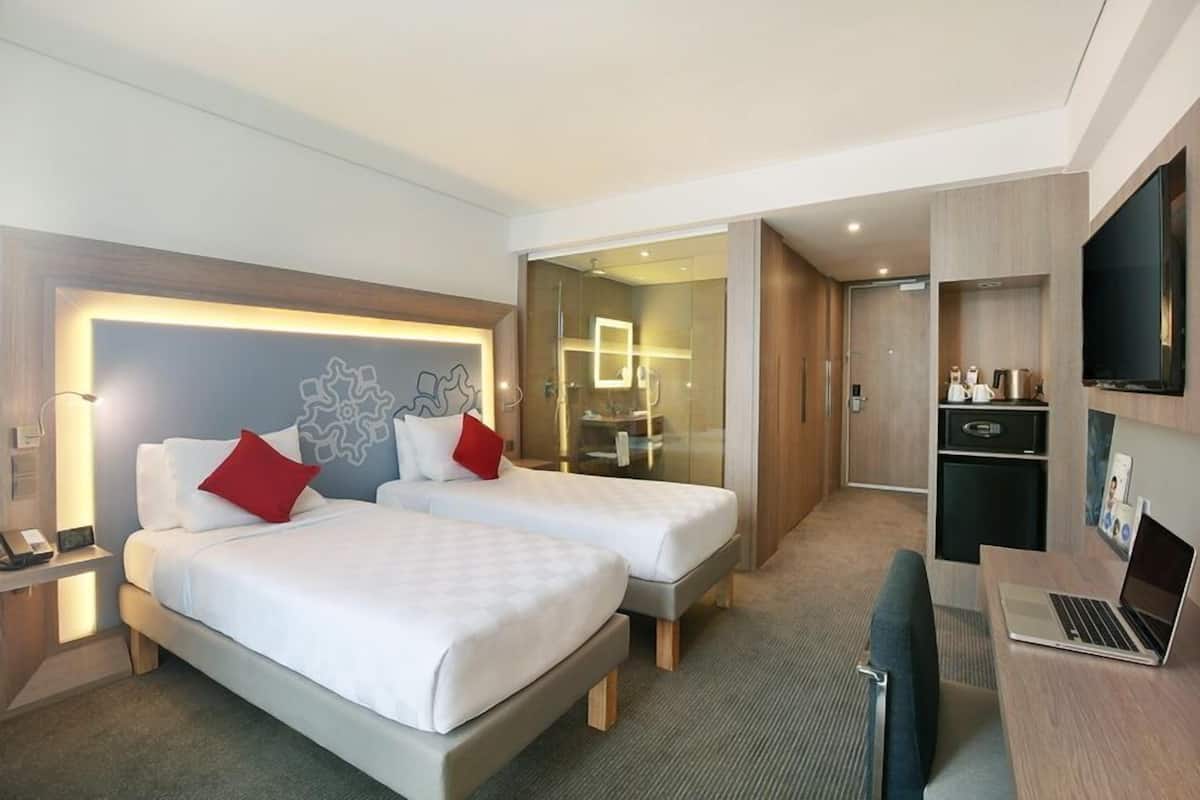 A hotel room with two beds, a desk with a laptop, a TV, and a minibar.