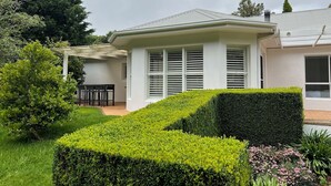 A modern house with a covered patio, neatly trimmed hedges, and a well-maintained garden. - Grounds of Robertson. Stylish and Exclusive. (Robertson)