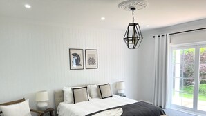 A bedroom with a large bed, two bedside tables with lamps, a bench, a white rug, and a view of greenery through a window. - Grounds of Robertson. Stylish and Exclusive. (Robertson)