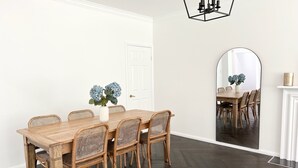 A dining room with a wooden table and wicker chairs, a white door, and a mirror reflecting the room. - Grounds of Robertson. Stylish and Exclusive. (Robertson)