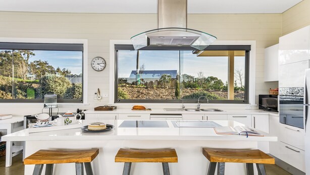 A modern kitchen with a large island, bar stools, a window with a view, and a clock on the wall. - The Junction Canyonleigh. Idyllic Weekends (Brayton)
