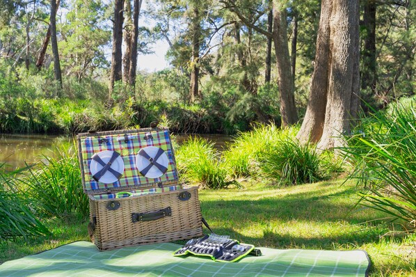 Un'area picnic con un cesto di vimini e una coperta a quadri vicino a un fiume, circondato da alberi.