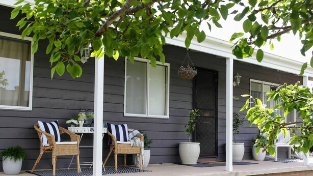 A porch with two wicker chairs, a small table, and potted plants. - Wine Country Cottage in the Southern Highlands (Welby)