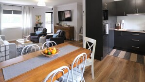 A modern living room with a dining table set for four, a kitchen with dark cabinets, and a flat-screen TV mounted on the wall. - Wine Country Cottage in the Southern Highlands (Welby)