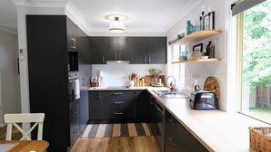 A modern kitchen with dark cabinets, a wooden countertop, and a window with a view of greenery. - Wine Country Cottage in the Southern Highlands (Welby)