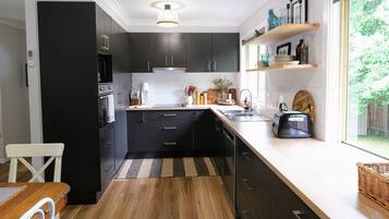 A modern kitchen with dark cabinets, a wooden countertop, and a window with a view of greenery.