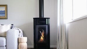 A modern living room with a black wood-burning stove, a grey sofa, and a wooden stool. - Wine Country Cottage in the Southern Highlands (Welby)