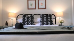 A neatly made bed with a black and white patterned headboard, two wall-mounted lamps, and a small vase with flowers on the nightstand. - Wine Country Cottage in the Southern Highlands (Welby)