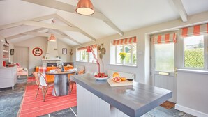 Una cocina amplia con una isla central, un comedor con sillas naranja y una alfombra roja.