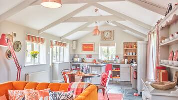 A cozy, well-lit kitchen with a dining area, featuring a red and white striped window valance, a clock, and a variety of kitchen utensils and appliances.