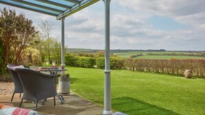 Un patio techado con muebles de mimbre y una mesa lista para comer, con vistas a un paisaje verde exuberante y viñedos.
