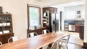 Une cuisine moderne avec une table et des chaises en bois, un réfrigérateur et une fenêtre équipée de stores.